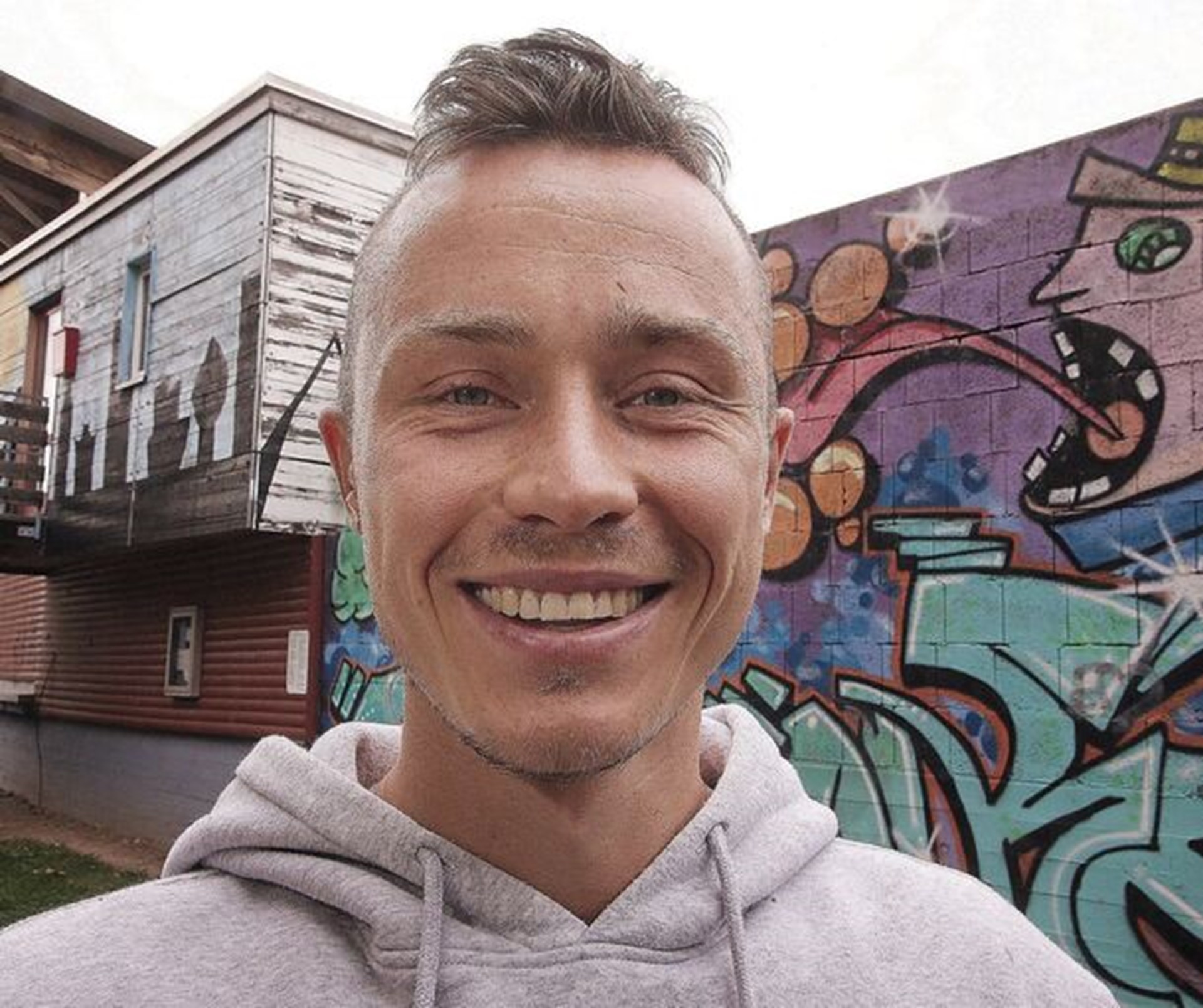 Lächelnder junger Mann steht vor Wand mit Graffiti